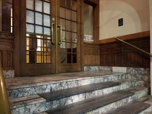 Entrance with wooden double doors and marble steps, featuring a sign for apartment access on the right.
