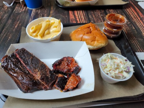 A tray with BBQ ribs, macaroni and cheese, a sandwich, coleslaw, and barbecue sauce cups.