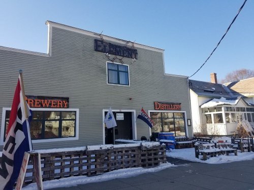 A building with signs for a brewery and distillery, surrounded by snow and flags, under a clear blue sky.