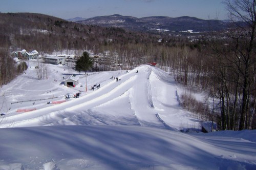 A snowy landscape with ski slopes, trees, and distant mountains under a clear blue sky.