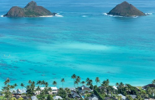A scenic view of two islands in turquoise waters, with lush greenery and palm trees in the foreground.