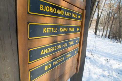 Wooden trail sign with multiple directional arrows for Bjorkland Lake, Kettle-Kame, Anderson Hill, and Big Woods trails.