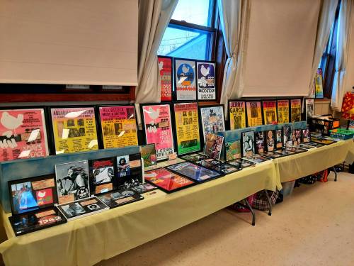 A display of colorful posters and memorabilia related to music festivals and artists, arranged on a table by a window.