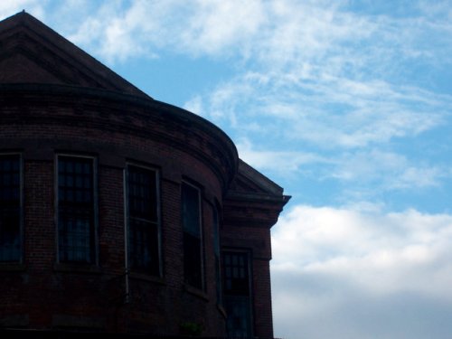 Silhouette of a brick building against a blue sky with scattered clouds.