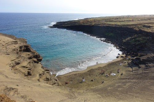 A scenic beach with golden sand and clear blue water, surrounded by rocky cliffs and a calm ocean.