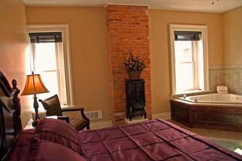 Cozy bedroom with a brick accent wall, large windows, a jacuzzi tub, and elegant furnishings.