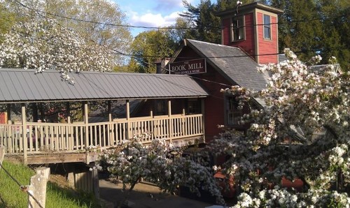 A historic red mill building surrounded by blooming trees and a wooden walkway.