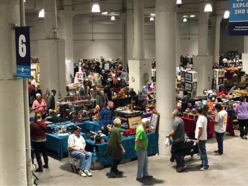 A bustling indoor market with numerous vendor booths and shoppers exploring various items for sale.