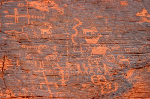 Petroglyphs on red rock, featuring abstract figures and symbols, showcasing ancient artistic expressions.