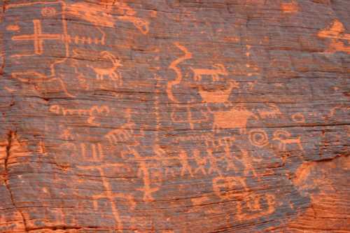 Petroglyphs on red rock, featuring abstract figures and symbols, showcasing ancient artistic expressions.