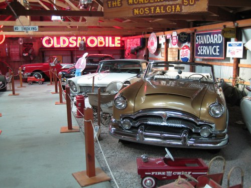 A vintage car museum featuring classic cars, neon signs, and nostalgic memorabilia in a rustic setting.