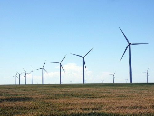 A row of wind turbines stands tall against a clear blue sky, set in a green field.