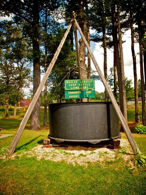 A large black kettle on a wooden frame, with a sign reading "World's Largest Kettle" surrounded by trees.