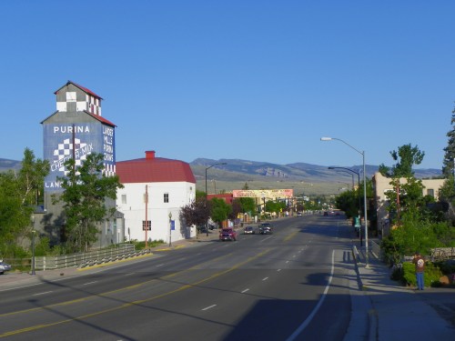 A quiet street scene featuring a Purina grain elevator, buildings, and mountains in the background under a clear blue sky.