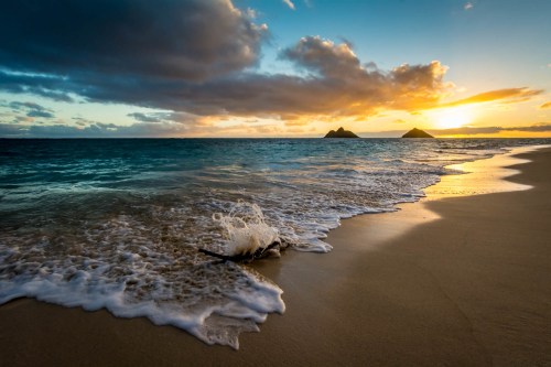 A serene beach at sunset, with gentle waves lapping at the shore and distant islands silhouetted against the colorful sky.
