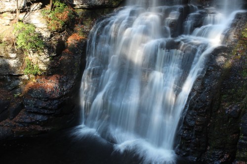 A serene waterfall cascading over rocky terrain, surrounded by lush greenery and dappled sunlight.