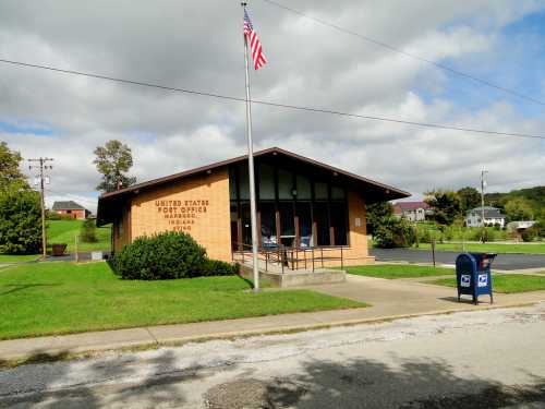 A small U.S. post office building with a flag, surrounded by green grass and a mailbox in front.