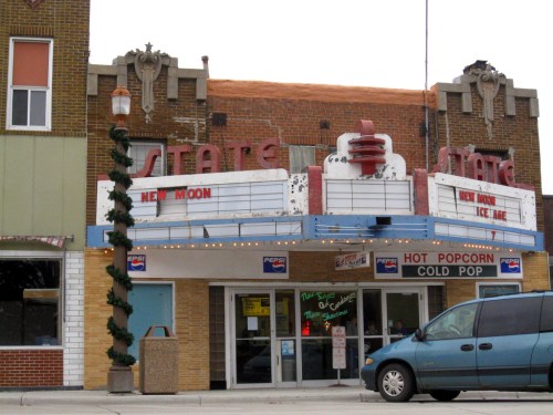 Historic movie theater with a marquee displaying "New Moon" and "Ice Age," featuring vintage architecture and a blue van parked outside.