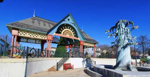 A colorful pavilion with a decorative roof and a sculpture in a park under a clear blue sky.