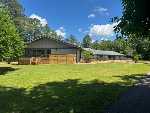 A spacious building surrounded by green grass and trees under a blue sky with fluffy clouds.