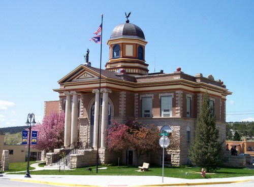 Historic building with a dome, columns, and flags, surrounded by trees and blooming flowers.