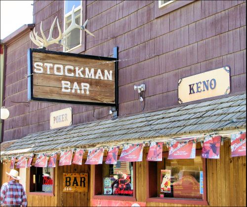Sign for Stockman Bar with Keno and Poker signs, featuring a rustic wooden facade and hanging banners.