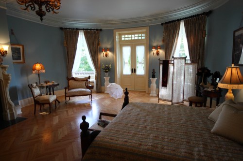 Elegant bedroom with blue walls, large windows, vintage furniture, and soft lighting, creating a cozy atmosphere.