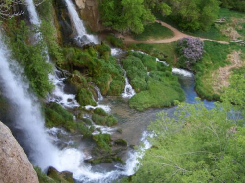 A scenic view of cascading waterfalls surrounded by lush greenery and a winding river below.