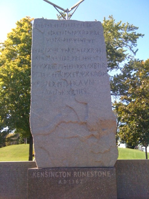 Kensington Runestone, a large stone with carved runes, surrounded by trees in a park setting.