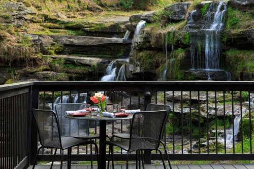 A cozy outdoor dining setup with a table and chairs overlooking a serene waterfall and lush greenery.