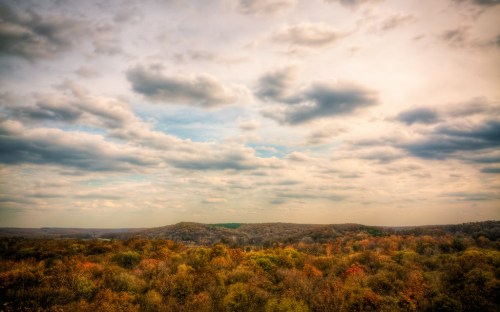 A scenic view of rolling hills covered in autumn foliage under a cloudy sky.