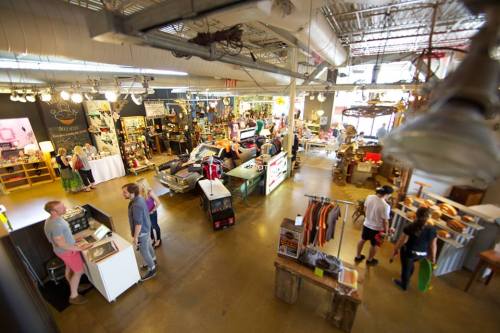 A spacious vintage store filled with various items, including furniture, clothing, and decor, with shoppers browsing around.