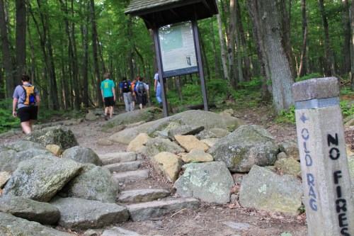 Hikers on a rocky trail in a forest, with a signpost indicating "Old Rag" and a warning about fire restrictions.