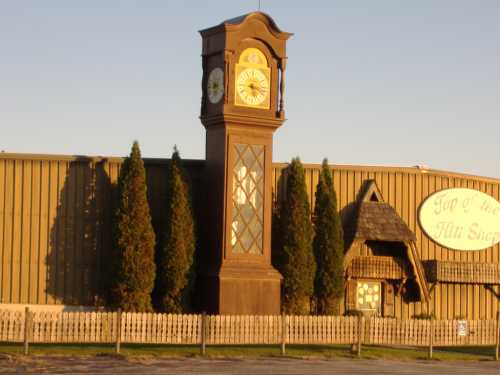 A large clock tower stands in front of a building, surrounded by trees and a white picket fence.