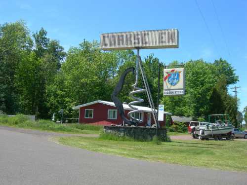 A roadside liquor store sign featuring a large spiral design, with a red house and trees in the background.