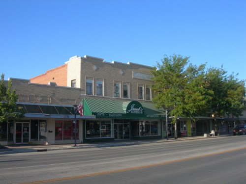 A charming downtown street scene featuring a green awning store, trees, and clear blue skies.