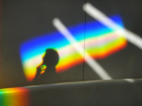 A silhouette of a person thinking, with colorful rainbow light reflections on a wall.