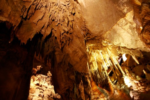 Stalactites and stalagmites in a dimly lit cave, showcasing intricate rock formations and textures.