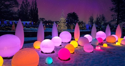 Colorful illuminated spheres and shapes in a snowy landscape, with a starry sky and festive lights in the background.