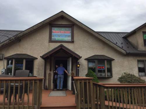 A man enters a restaurant with a welcoming sign and "OPEN" neon light, surrounded by greenery and cloudy skies.