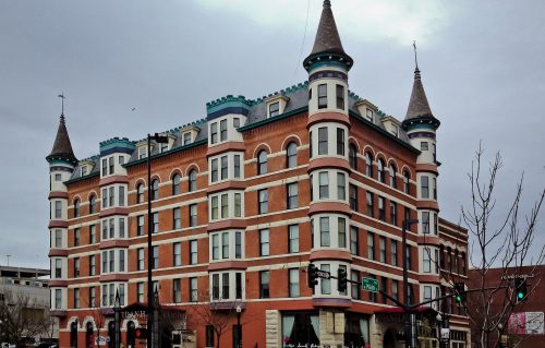 Historic brick building with turrets and decorative trim, featuring a mix of red and white colors, under a cloudy sky.