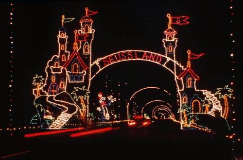 Colorful illuminated archway reading "Seussland," featuring whimsical towers and festive decorations at night.