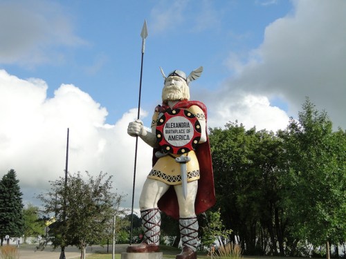 A large statue of a Viking holding a spear, wearing a cape, with a sign reading "Alexandria, Birthplace of America."