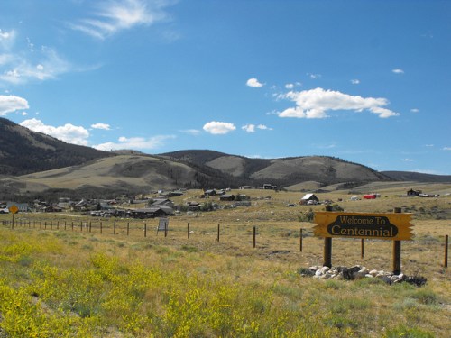 A scenic view of Centennial, Wyoming, featuring a welcome sign, mountains, and a grassy landscape under a blue sky.