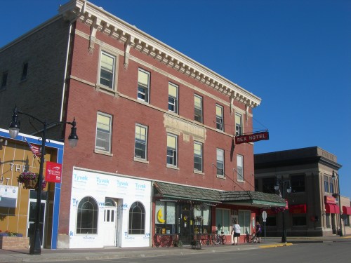 Historic brick building with a sign reading "B.E.X. Hotel," featuring storefronts and a clear blue sky.