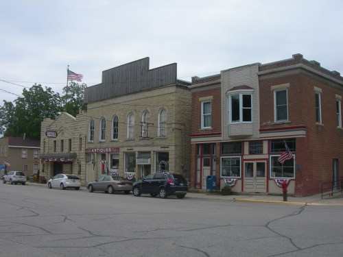 A quaint street scene featuring historic buildings, flags, and parked cars in a small town.