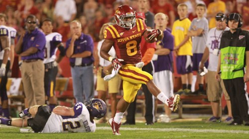A football player in a red and gold uniform runs past a tackled opponent on the field during a game.