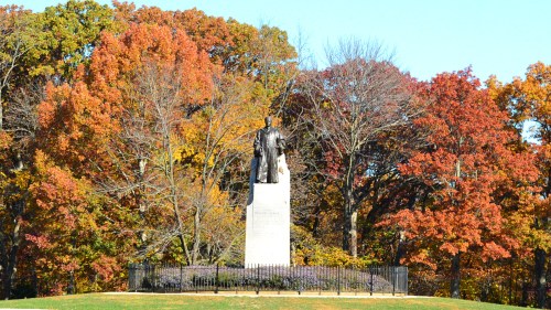 A statue on a pedestal surrounded by vibrant autumn trees with colorful leaves.
