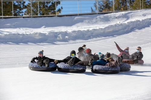 A group of people enjoying snow tubing on a snowy slope, laughing and having fun on a sunny day.