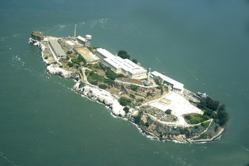 Aerial view of Alcatraz Island, featuring buildings and rocky shoreline surrounded by water.